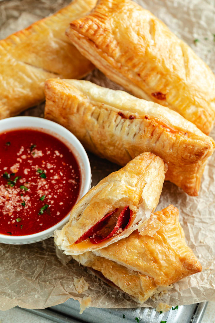 Golden air fryer pizza pockets arranged on parchment paper with a bowl of marinara sauce for dipping.