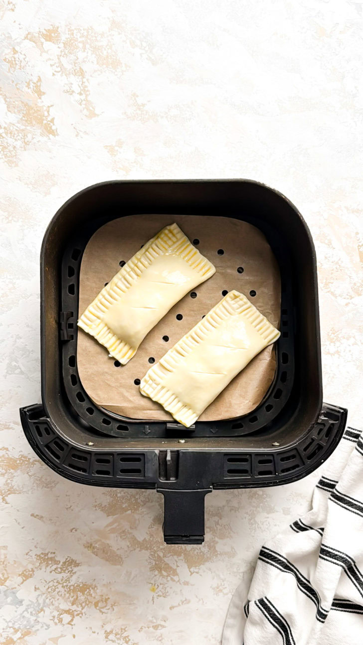 Unbaked air fryer pizza pockets on parchment inside an air fryer basket, ready to cook.