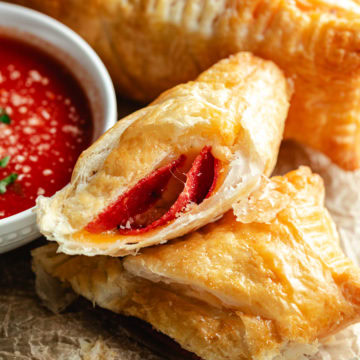 Close-up of crispy air fryer pizza pockets filled with pepperoni and melted cheese next to a bowl of marinara sauce.