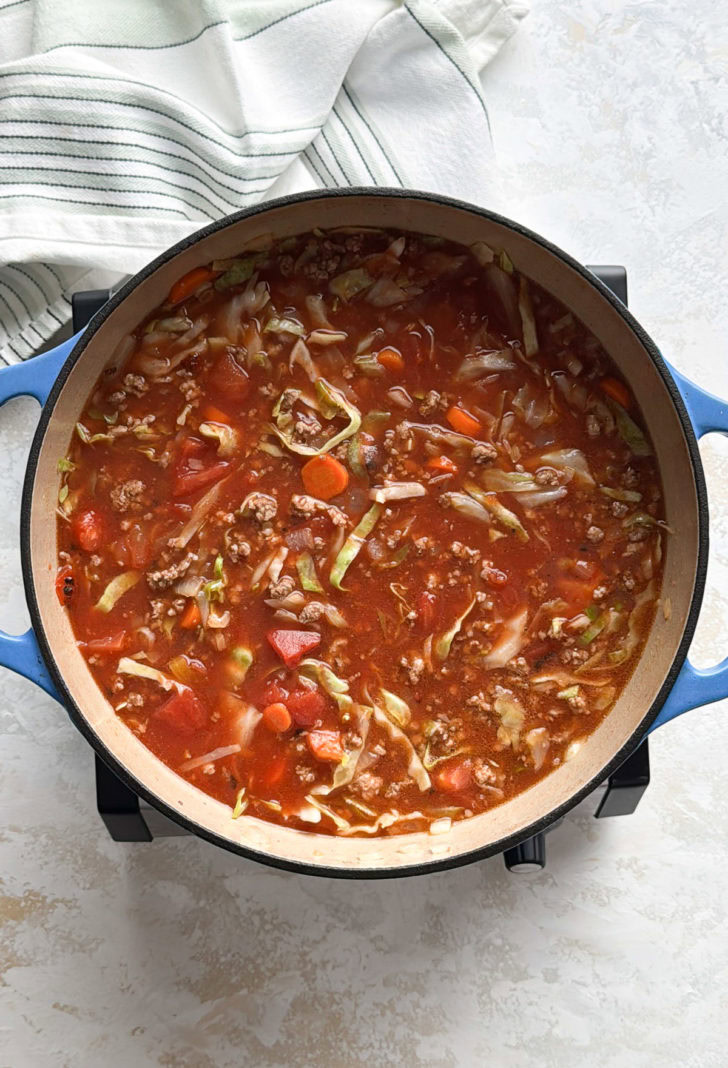 Blue Dutch oven filled with tomato-based soup with cabbage, carrots, and ground beef.
