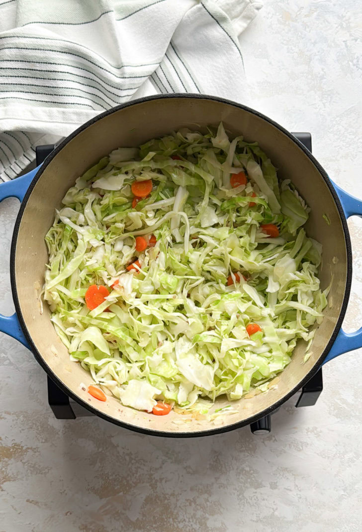 Shredded cabbage and carrot slices cooking down in a large Dutch oven.