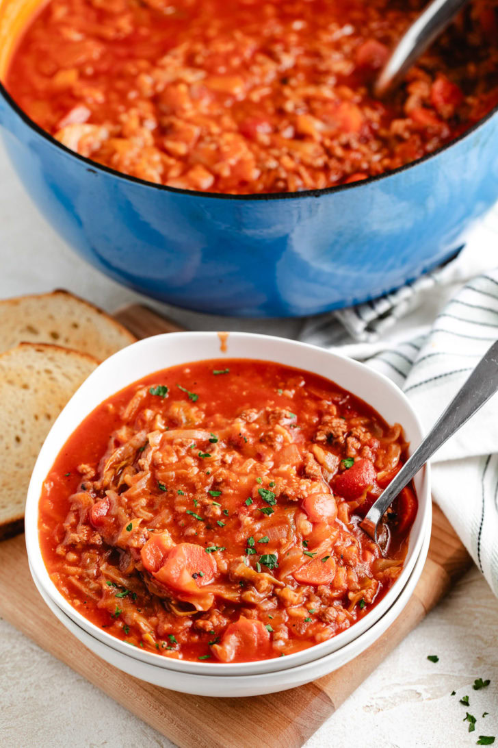 A bowl of cabbage roll soup in front of a blue Dutch oven.