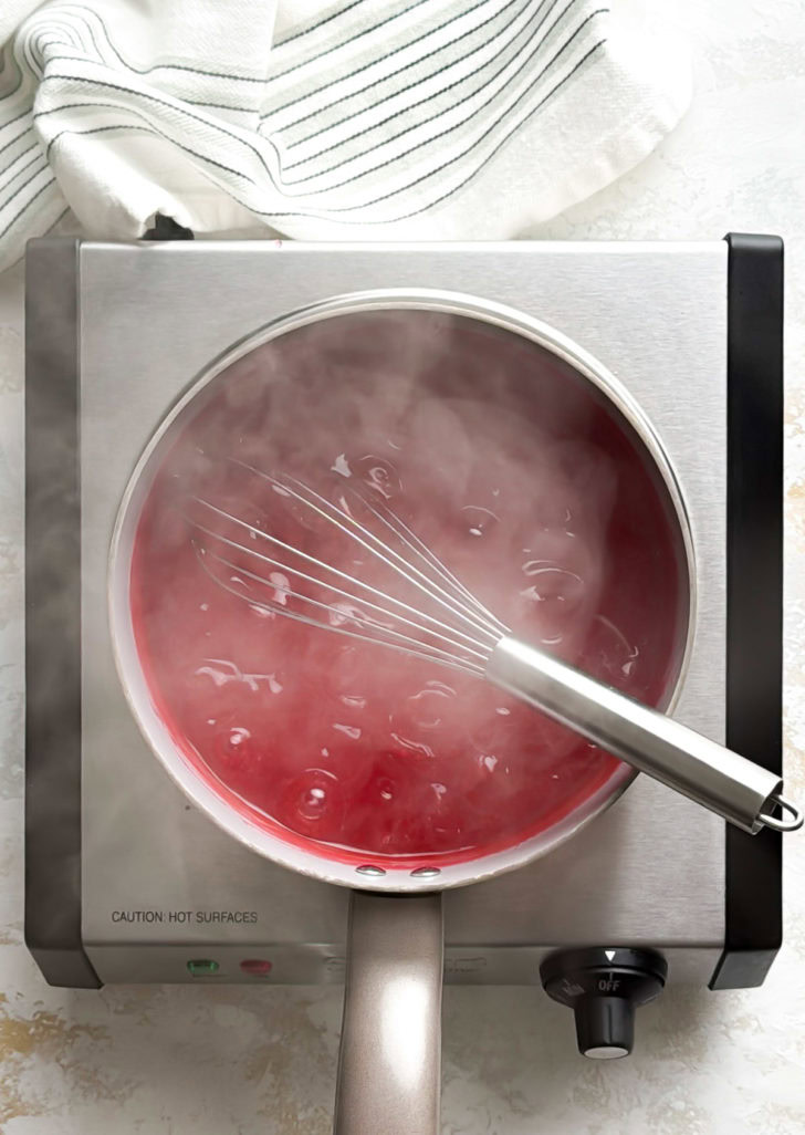 Thickened fresh strawberry pie glaze bubbling and steaming in a saucepan.