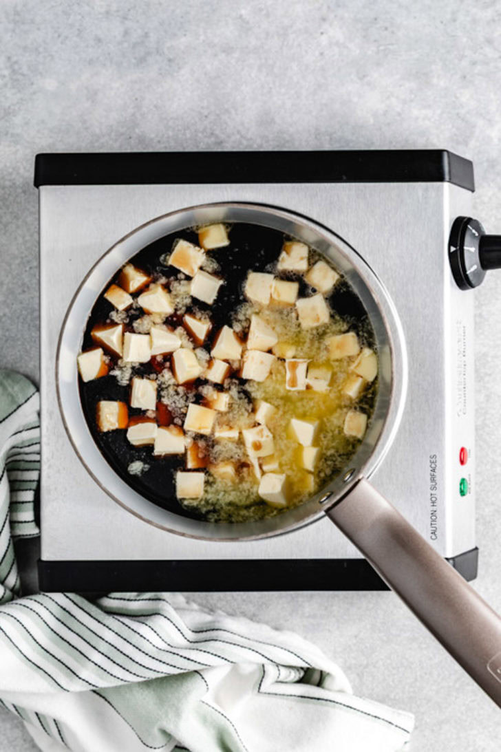 Butter cubes melting into dark Guinness stout in a saucepan on a countertop burner for chocolate cake with Guinness.