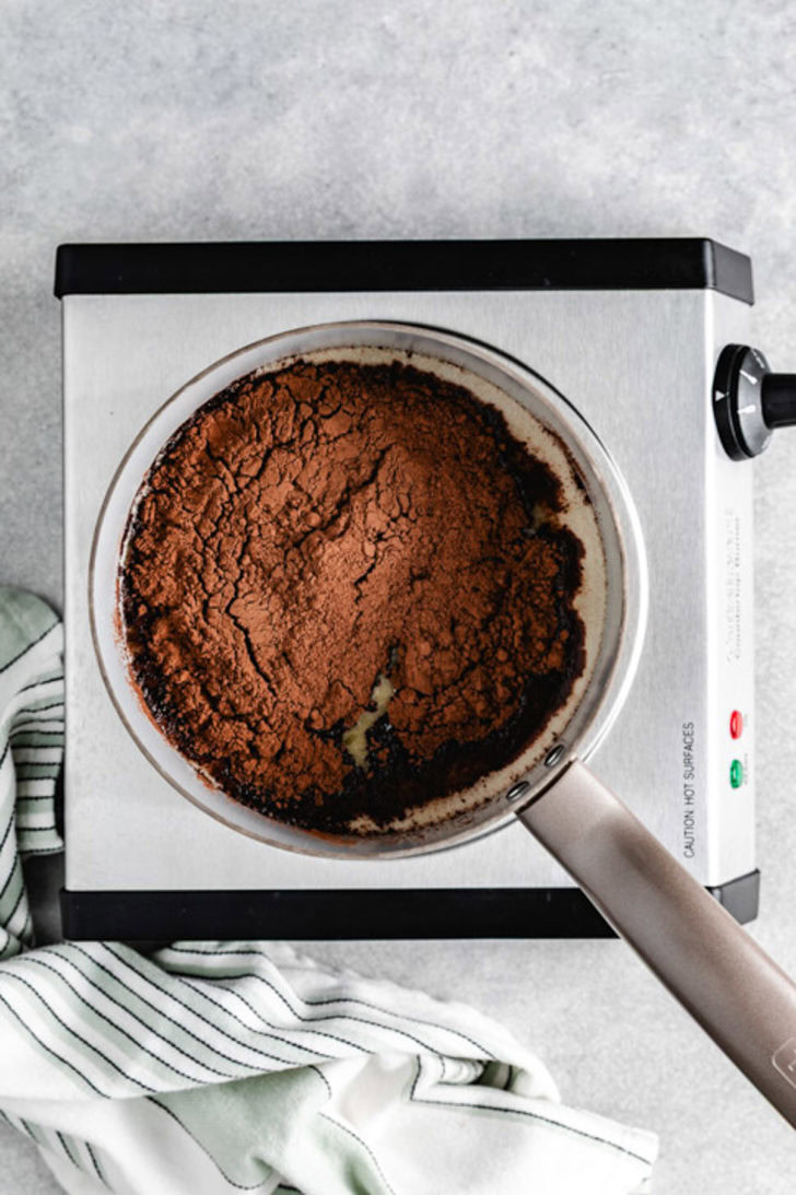 Saucepan filled with warm Guinness and a layer of unsweetened cocoa powder ready to whisk into a chocolate cake base.