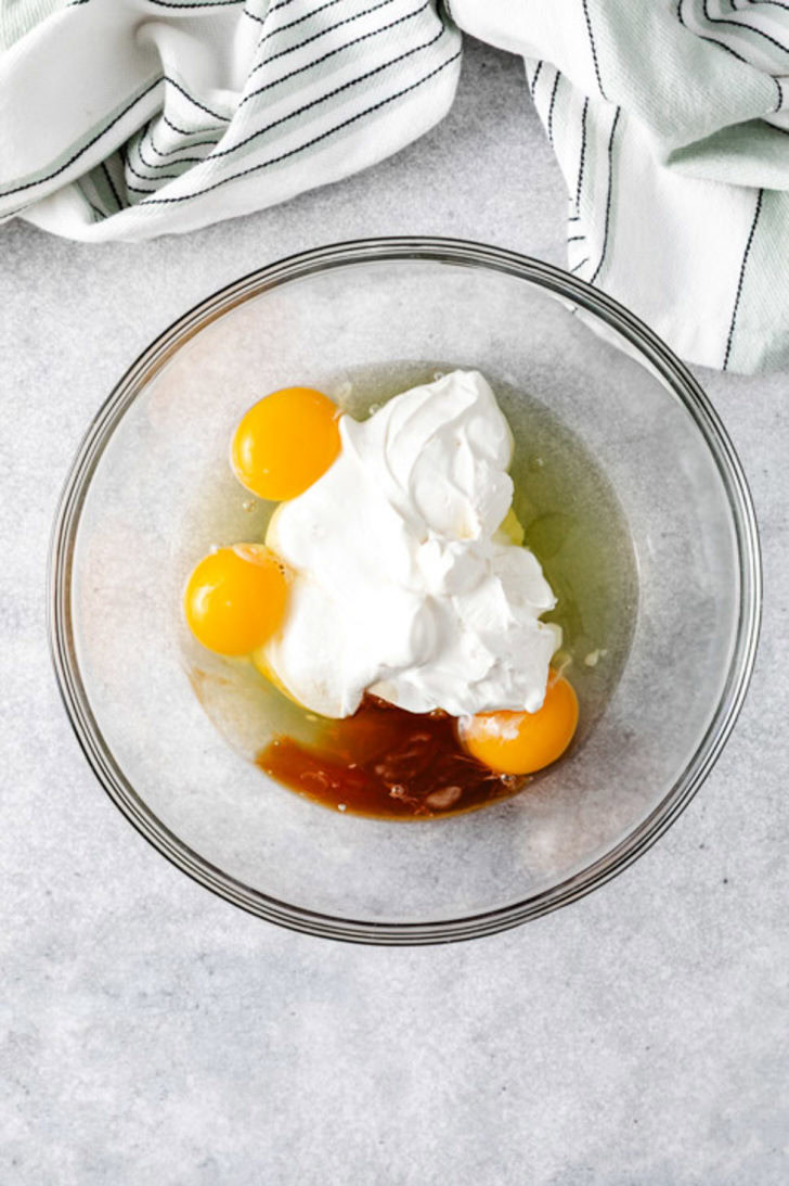 Glass mixing bowl with eggs, sour cream, and vanilla extract ready to be whisked together for the cake batter.