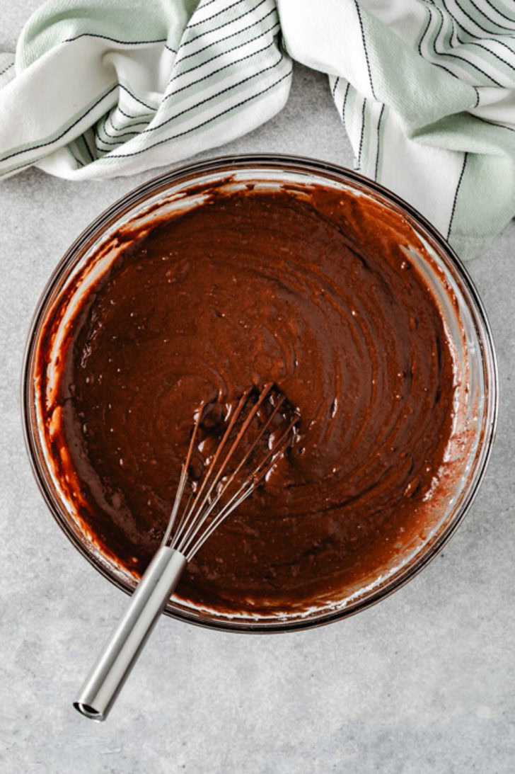Thick chocolate cake with Guinness batter in a glass mixing bowl with a metal whisk.