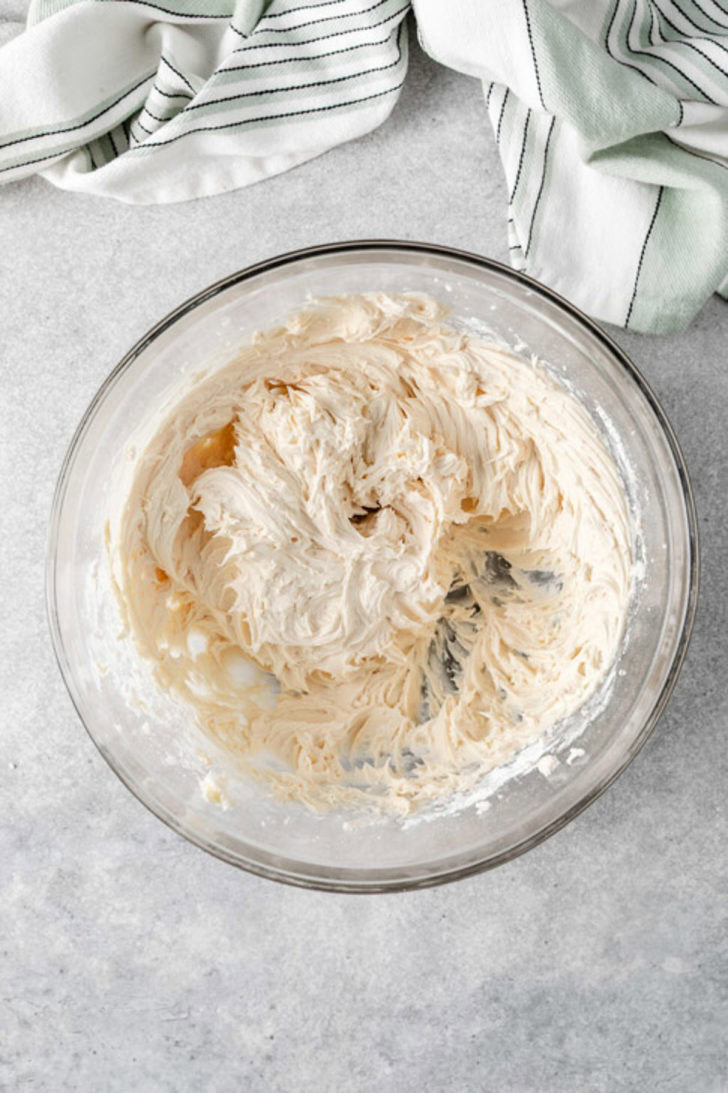 Smooth Baileys buttercream frosting whipped in a clear glass bowl on a light countertop.
