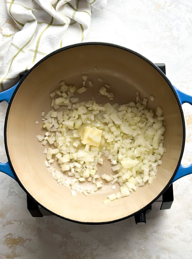 Onions and butter sautéing in a blue Dutch oven.