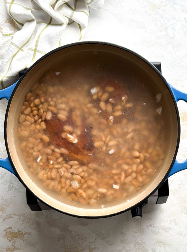 Pinto beans simmering in a Dutch oven with ham hocks and broth.