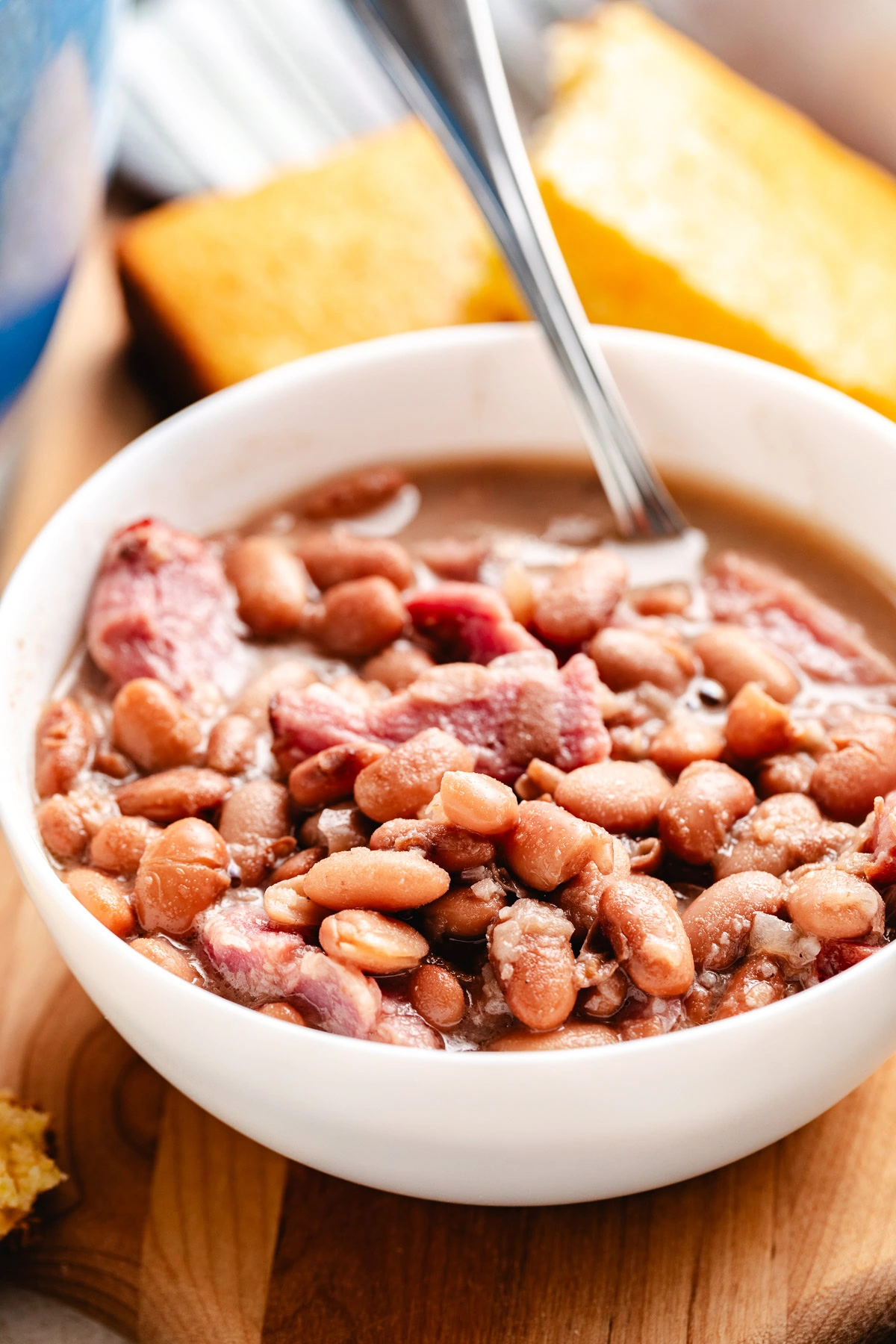Close-up of pinto beans and ham in a white bowl on a wooden board.