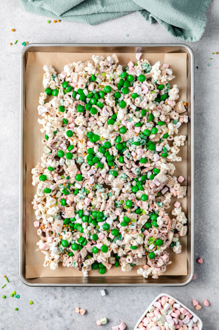 Tray of leprechaun bait snack mix spread on parchment and topped with extra green candies and marshmallows.