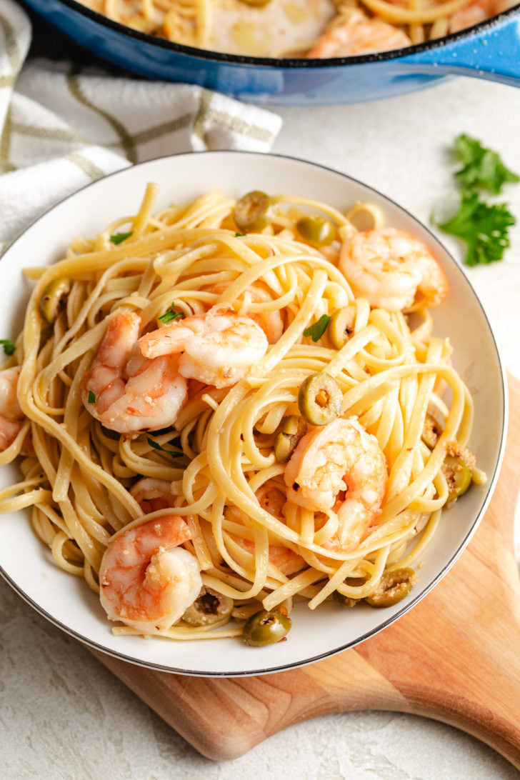 Skillet of mediterranean shrimp pasta next to a serving bowl.