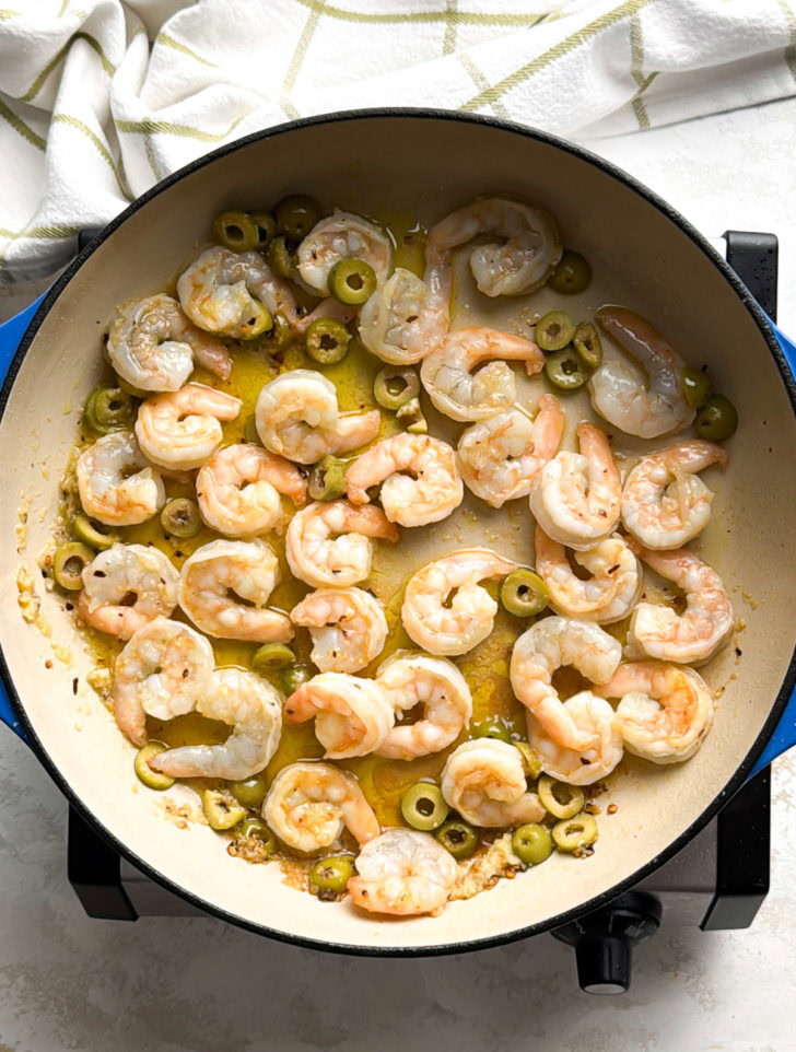 Shrimp and green olives simmering in olive oil in a skillet.