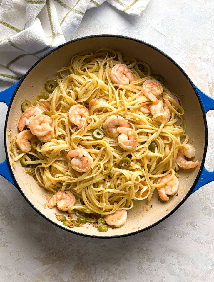 Skillet filled with mediterranean shrimp pasta and green olives viewed from above.