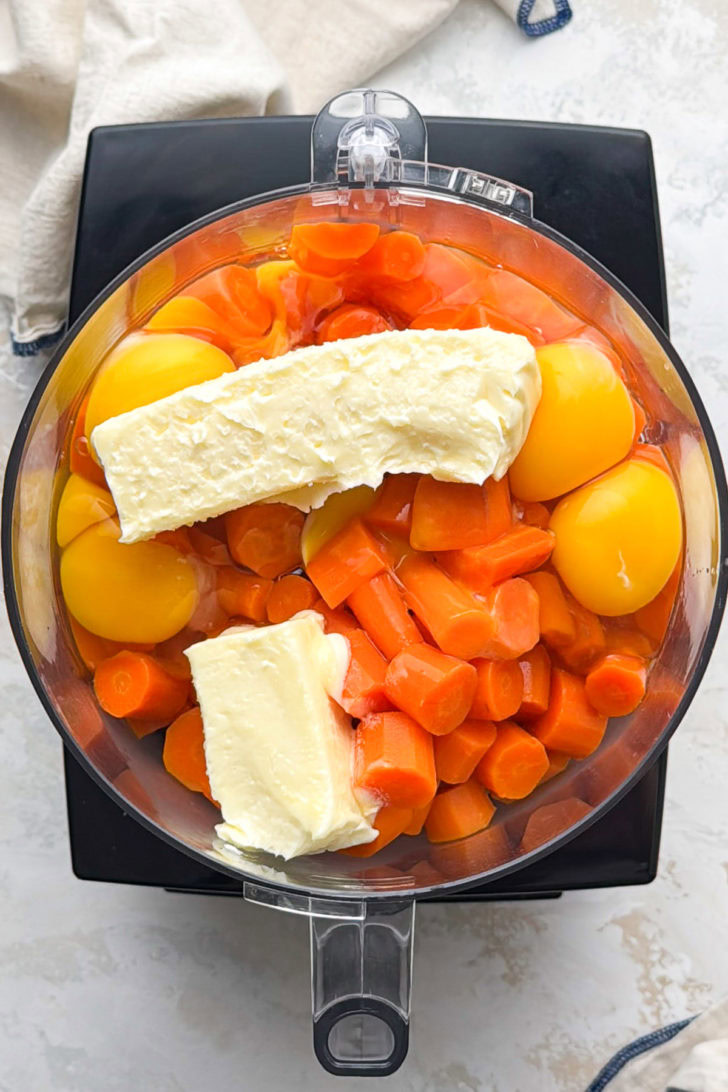 Cooked carrots, eggs, and butter sit in a food processor bowl.