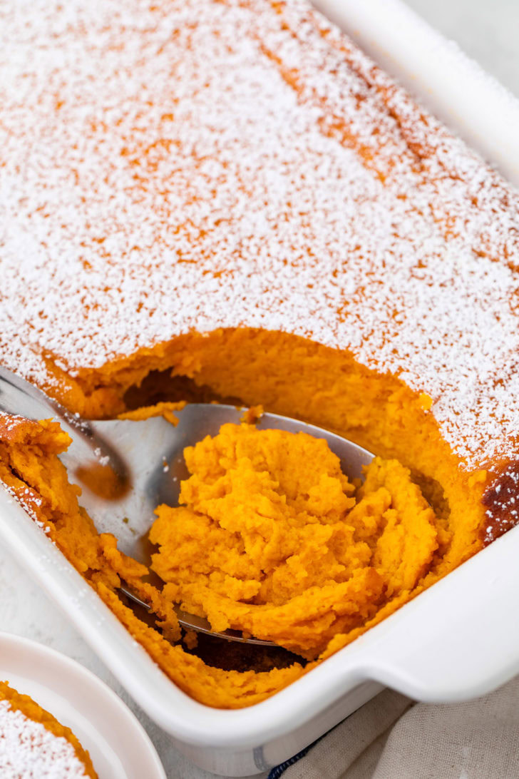 A serving spoon lifts carrot soufflé from the baking dish.