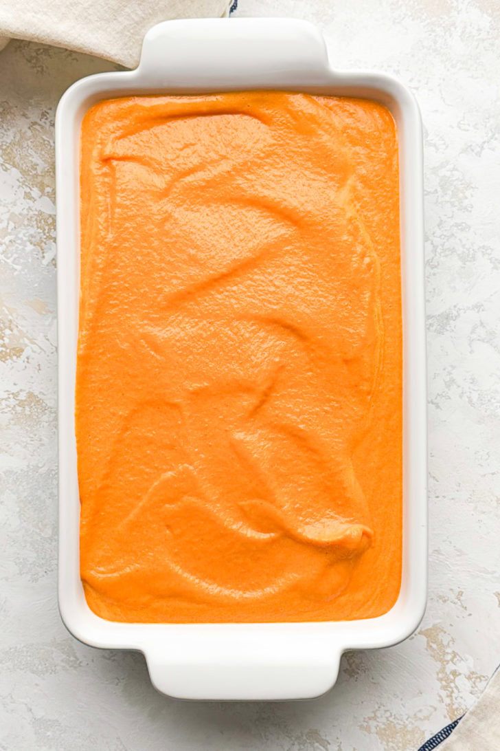 Carrot soufflé batter is spread into a white baking dish.