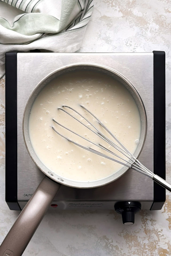 Milk, cream, and cream of coconut are whisked together in a saucepan.