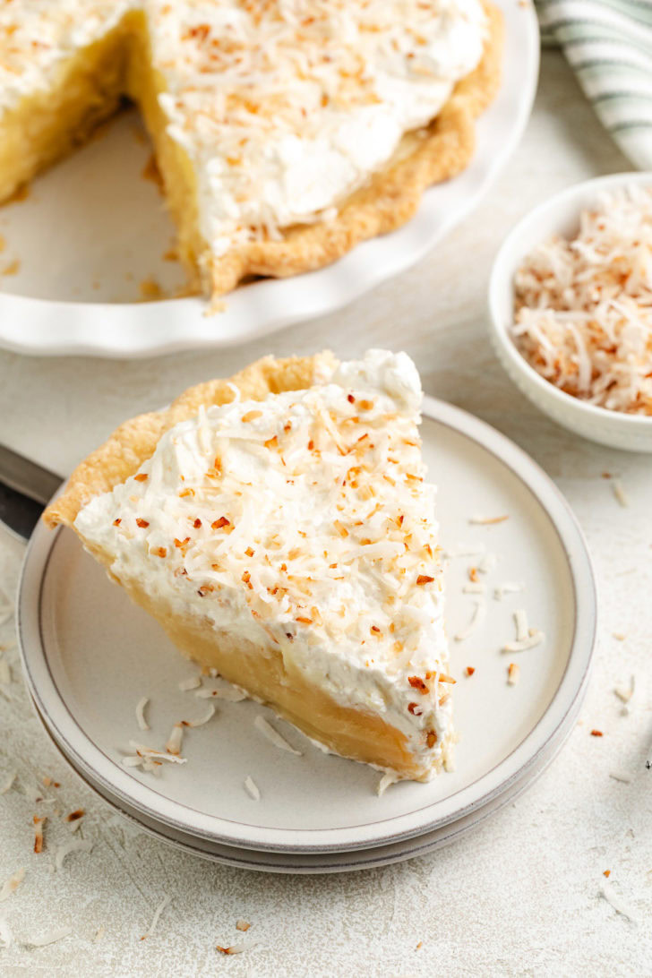 A plated slice is shown in front of the pie dish and a bowl of toasted coconut.