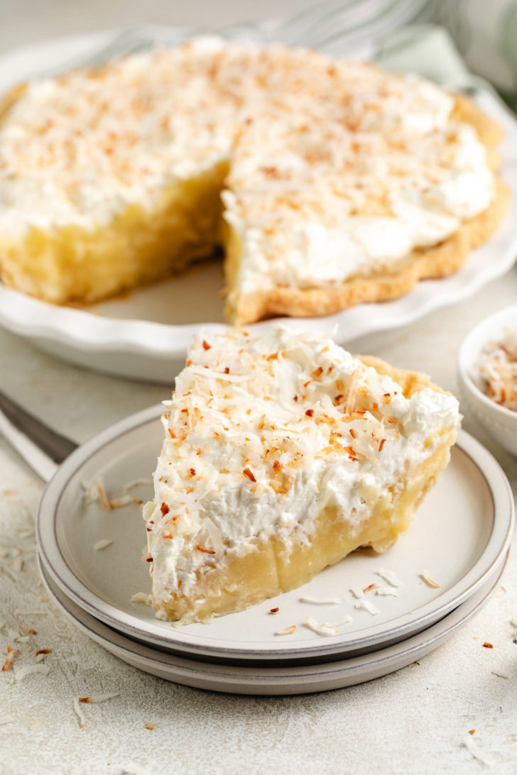 A slice of pie is centered on a plate with the whole pie behind it.