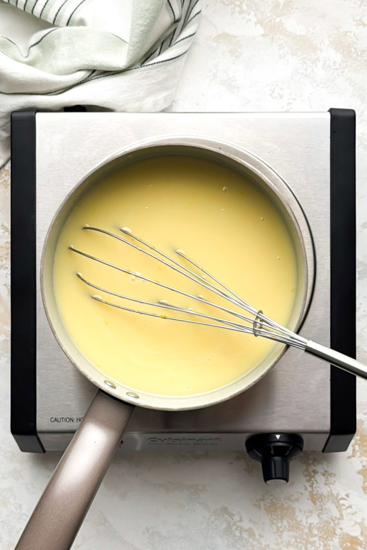 The custard mixture cooks in a saucepan with a whisk.