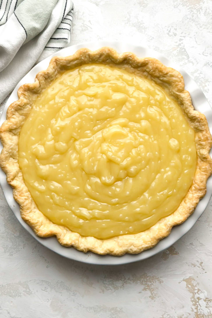 Coconut cream pie filling is spooned into a baked pie crust.