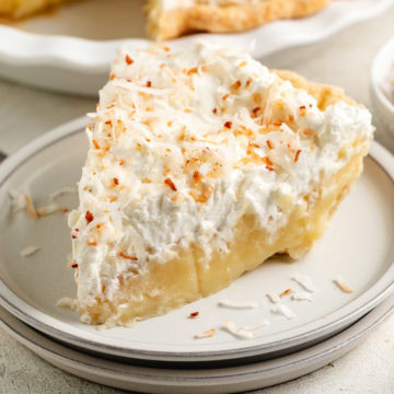 A slice of coconut cream pie topped with whipped cream and toasted coconut sits on a plate.