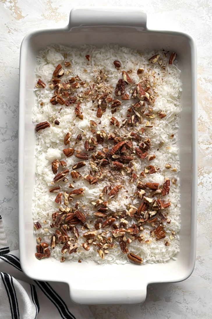Coconut flakes and pecans in a baking dish.