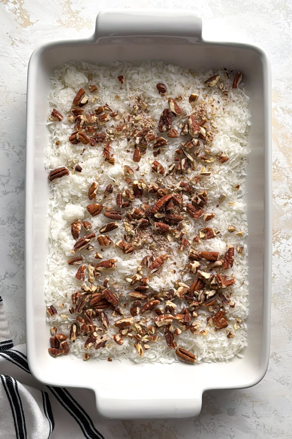 Coconut flakes and pecans in a baking dish.
