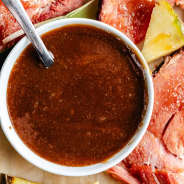 Glaze for ham in a white bowl with sliced ham and pineapple.