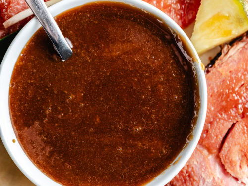 Glaze for ham in a white bowl with sliced ham and pineapple.