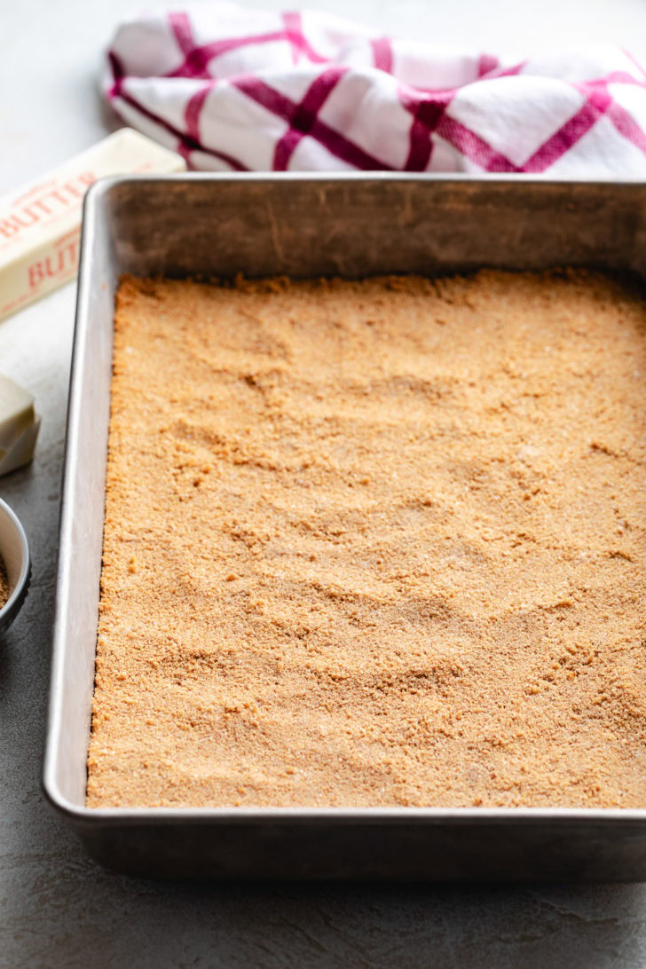 The textured surface of a tightly packed dessert base is ready for the oven.
