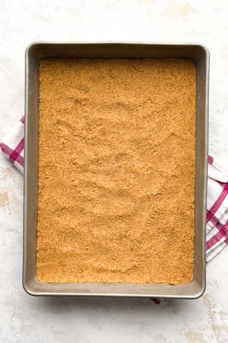 An overhead view shows a perfectly even graham cracker crust covering the bottom of a pan.