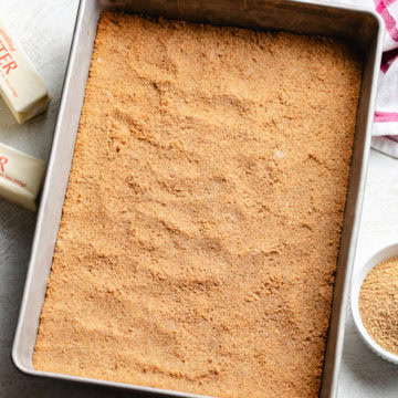 A fully pressed homemade graham cracker crust rests in a rectangular baking pan.