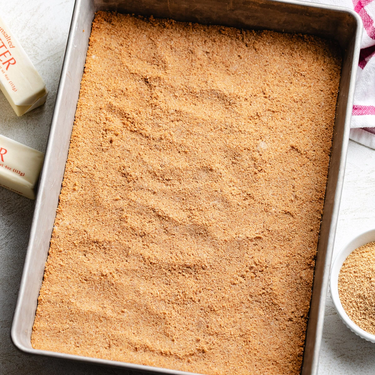 A fully pressed homemade graham cracker crust rests in a rectangular baking pan.