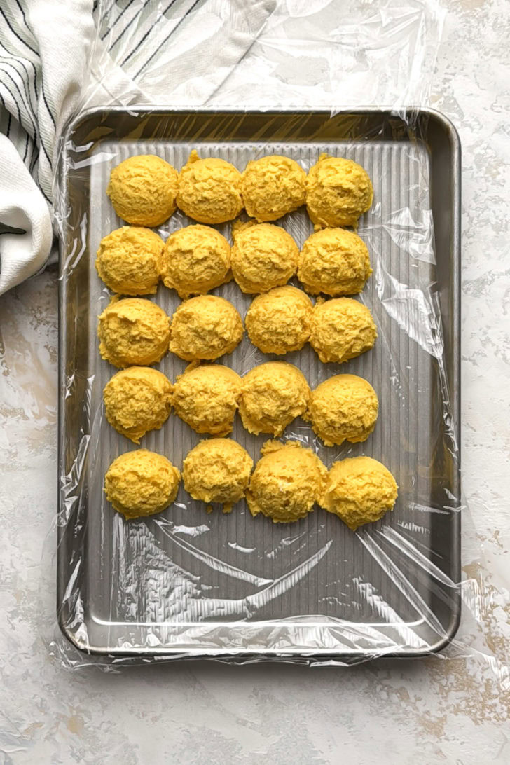 Scooped lemon crinkle cookies chilling on a sheet pan.