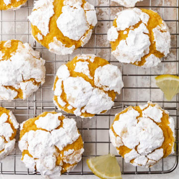 Lemon crinkle cookies on a cooling rack with lemon wedges.