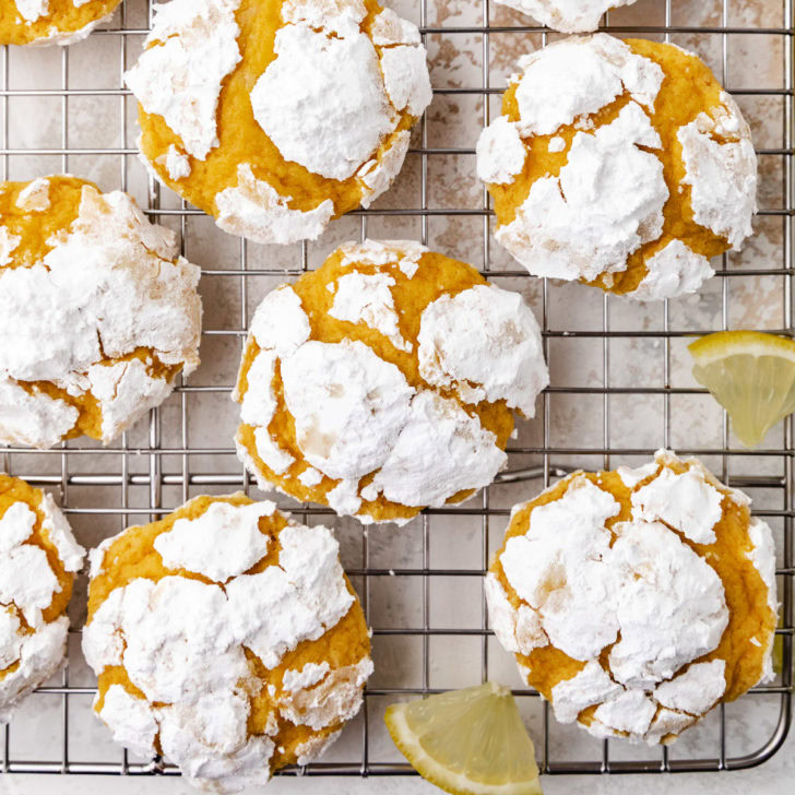 Lemon crinkle cookies on a cooling rack with lemon wedges.
