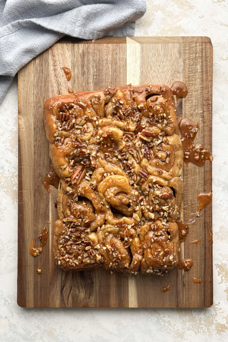 Pecan sticky buns turned out onto a wooden board with caramel sauce pooling around the edges.