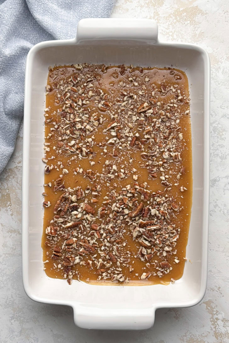 Chopped pecans sprinkled over the brown sugar caramel topping in a greased 9x13 baking dish.