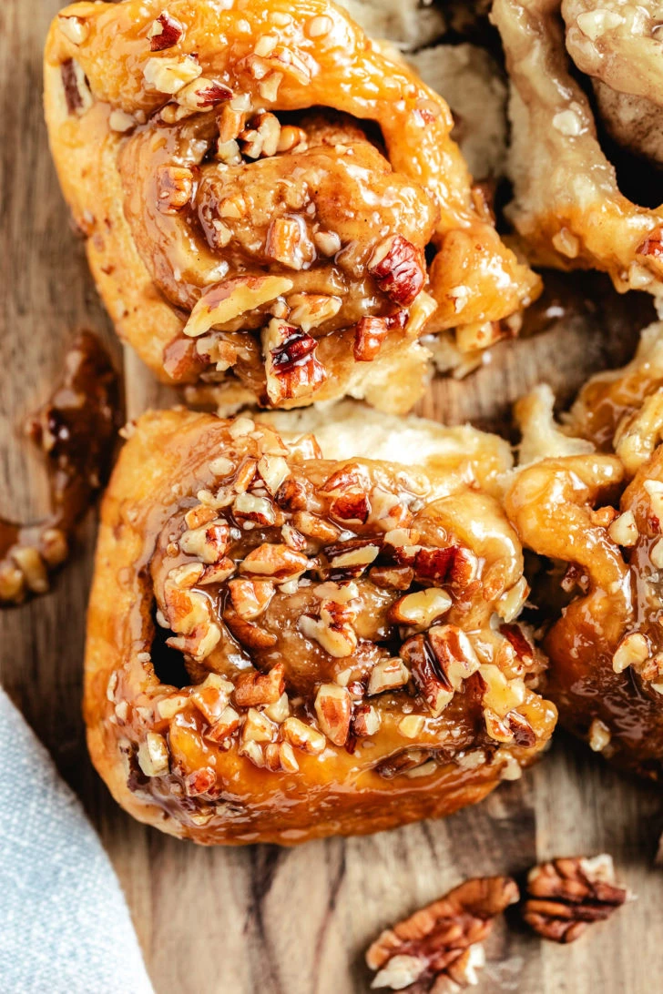 Close-up of one pecan sticky bun with glossy caramel sauce drizzled over the top.