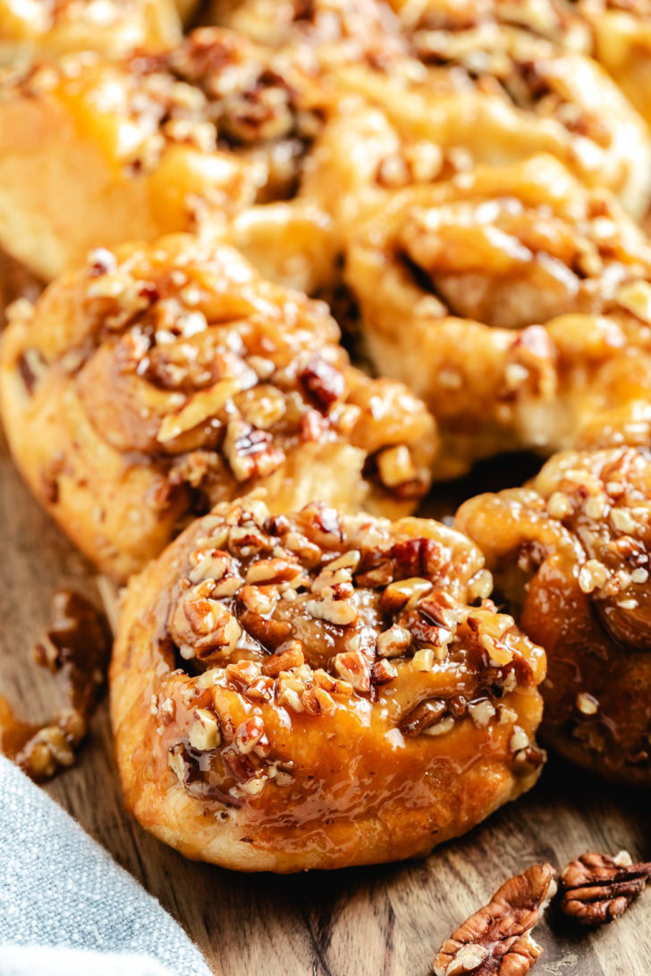 Sticky buns with Rhodes cinnamon rolls, chopped pecans, and glossy caramel topping on a wooden board.