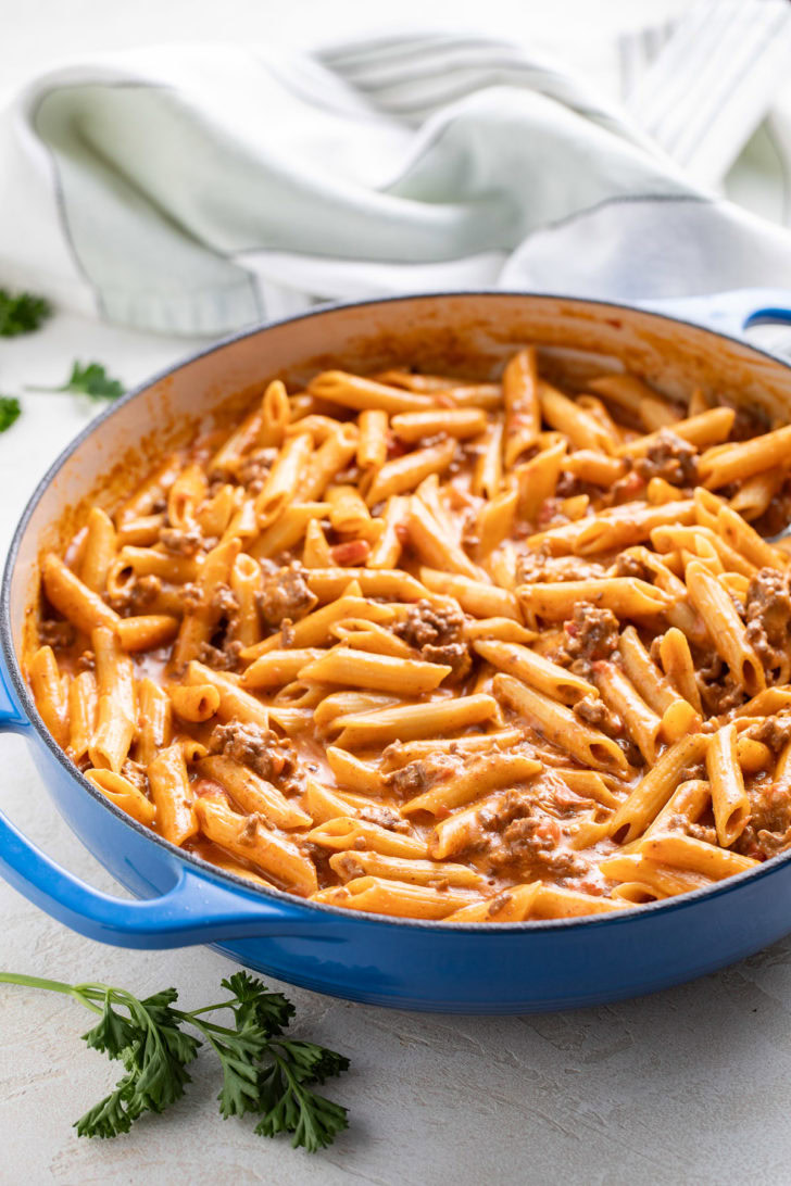 Taco penne pasta in a blue skillet with parsley nearby.