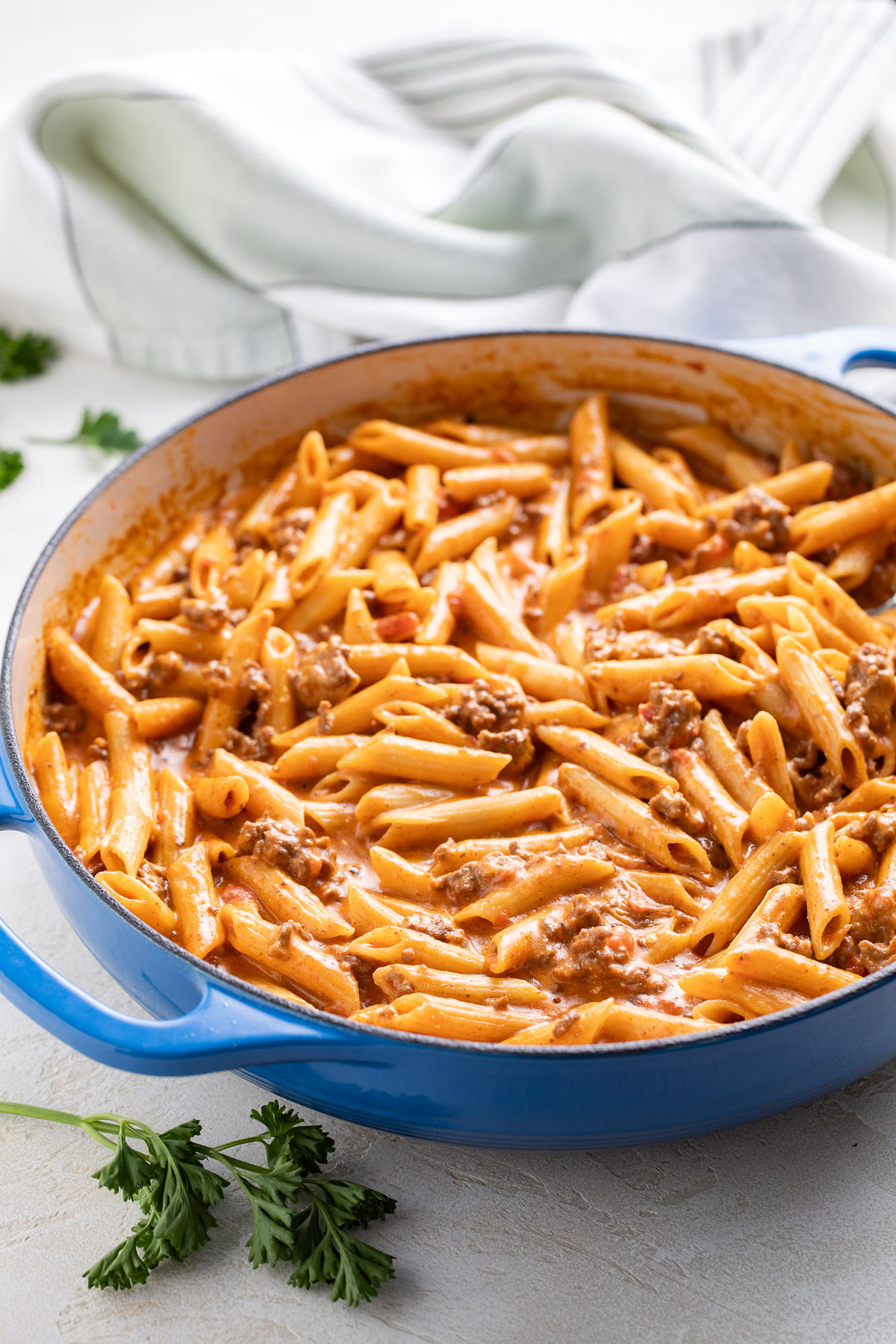 Taco penne pasta in a blue skillet with parsley nearby.