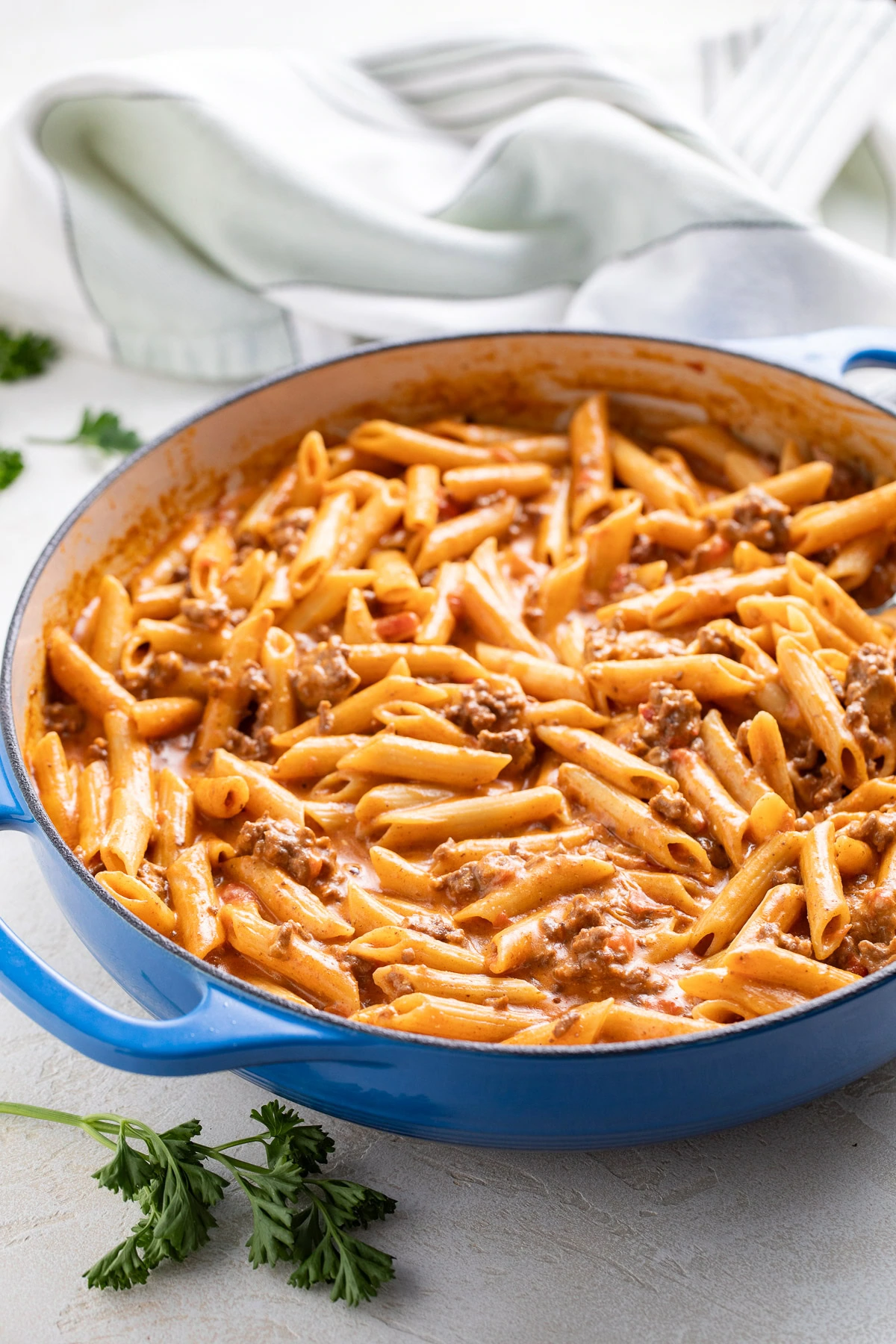 Taco penne pasta in a blue skillet with parsley nearby.