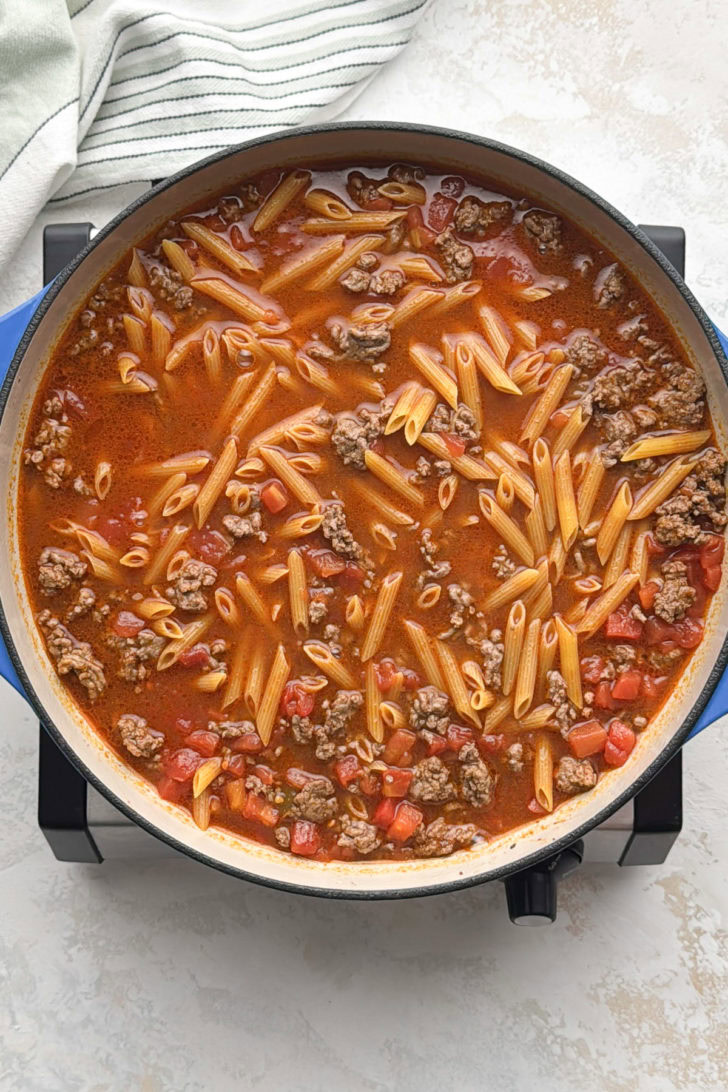 Penne simmering with ground beef and tomatoes in broth.
