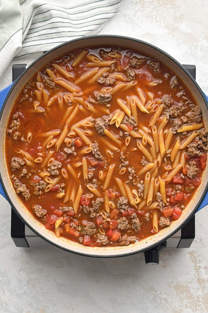 Penne simmering with ground beef and tomatoes in broth.