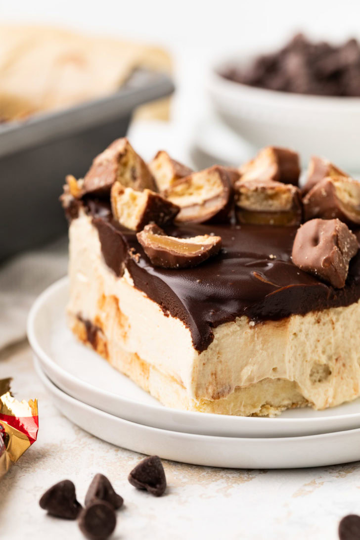 Close-up of a cheesecake bar slice with ganache and chopped candy bars on top.
