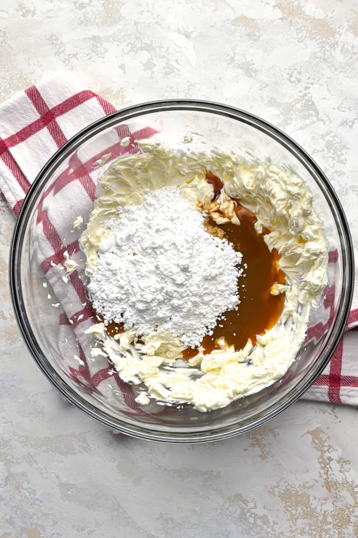 Cream cheese, caramel sauce, and powdered sugar in a mixing bowl.